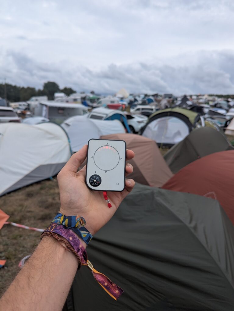Person holding Buddycompass festival tracker at campsite.