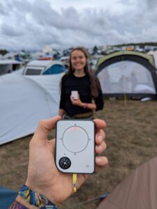 Person holding Buddycompass festival tracker at campsite.